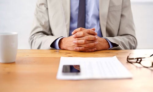 Mann sitzt mit verschränkten Armen an einem Holztisch